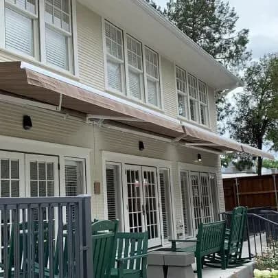 A partially-extended retractable awning over the patio of a beige house.