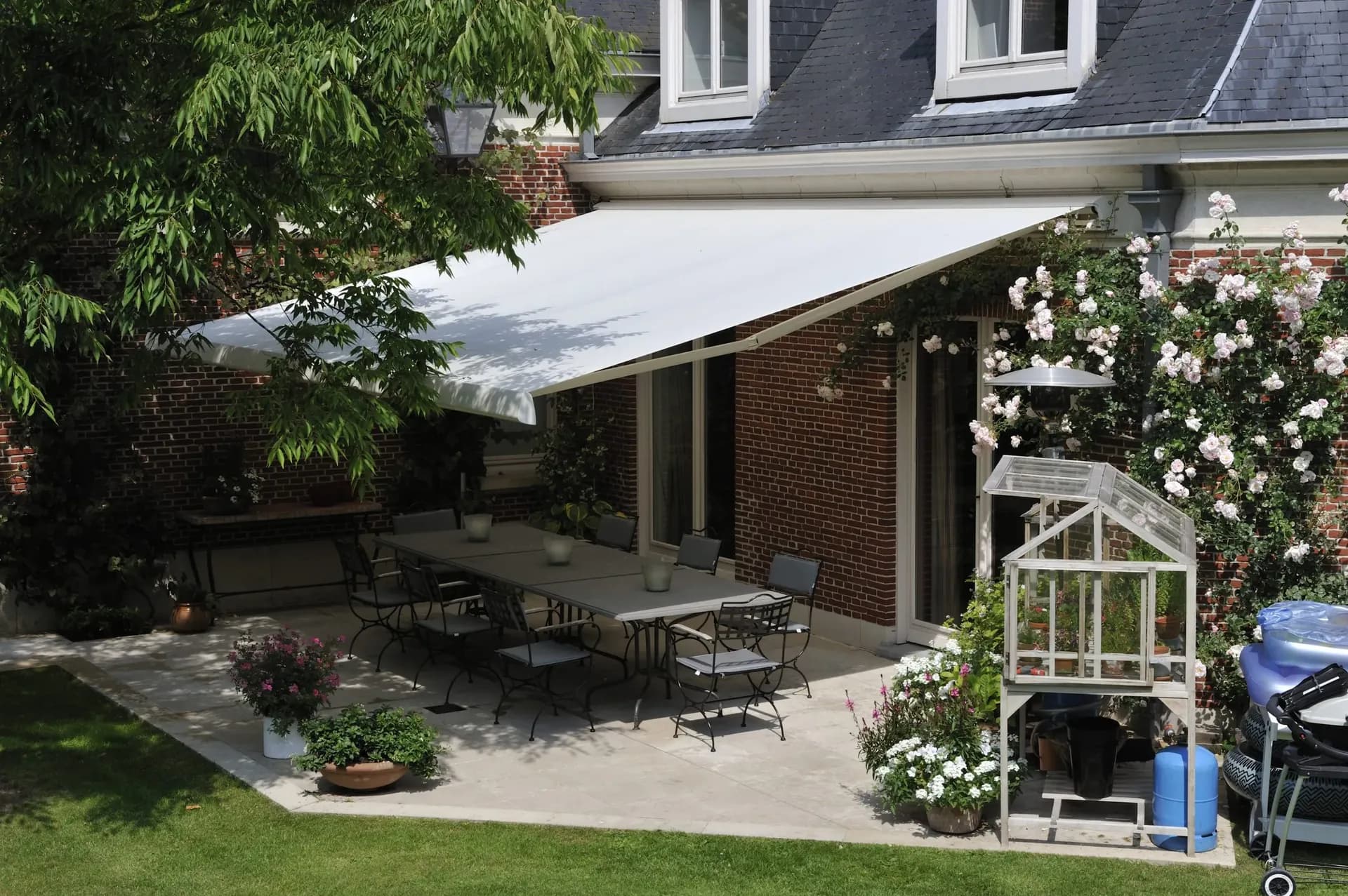 A white retractable awning covers a patio off a red brick house.