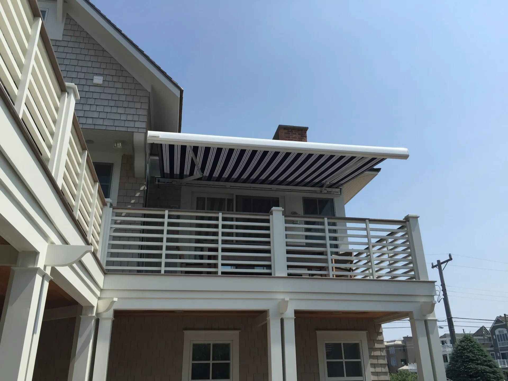 An upward-looking view of a second-floor porch with a blue and white striped retractable awning.