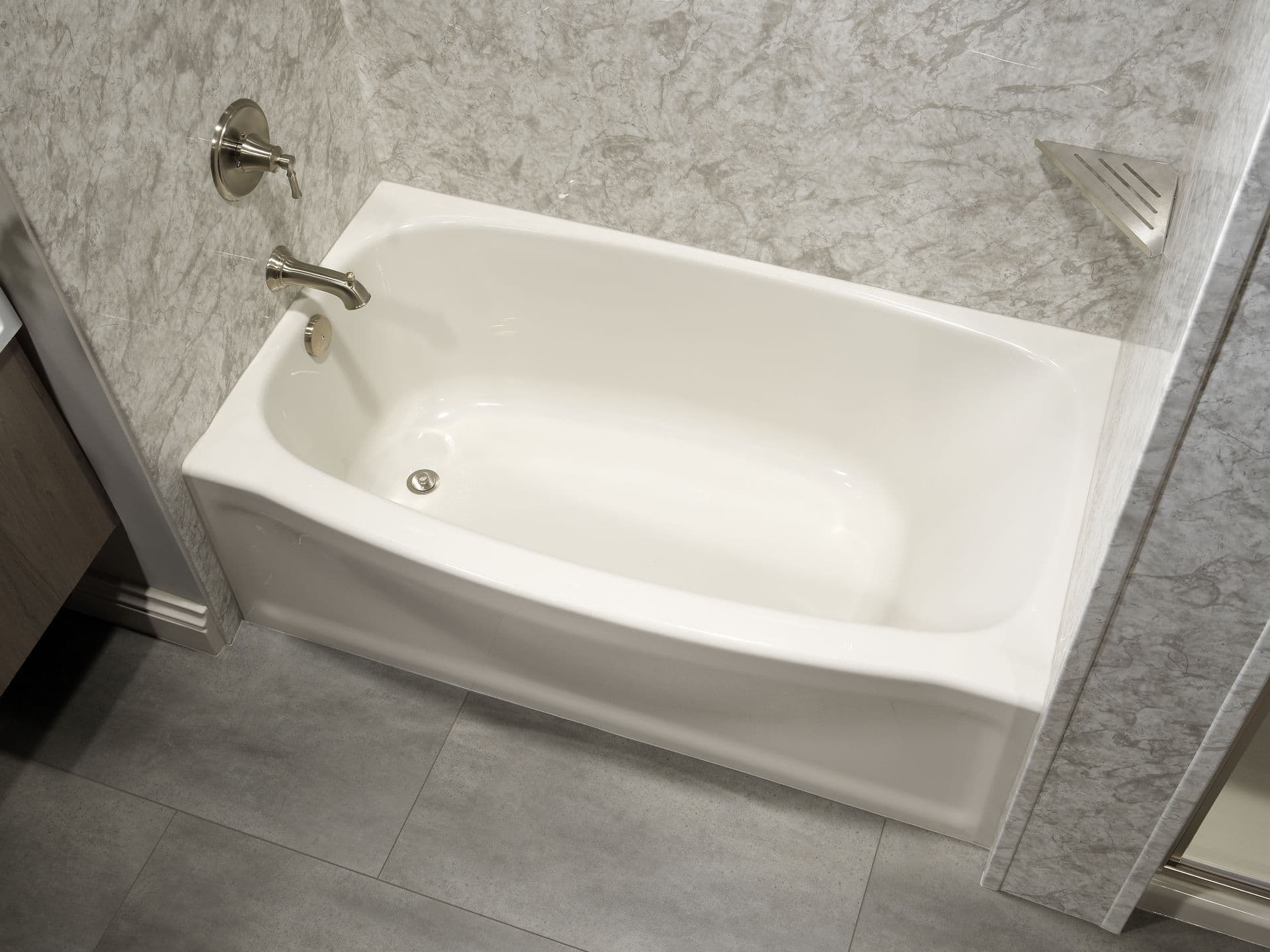 An overhead view of a new white bathtub with gray marbled walls and brushed metal fixtures.