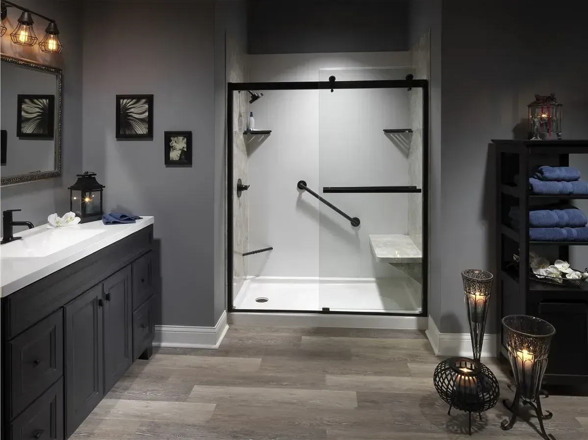 A gray bathroom with white walk-in shower with sliding glass doors, matte black fixtures, built-in seat bench, and grab bar.