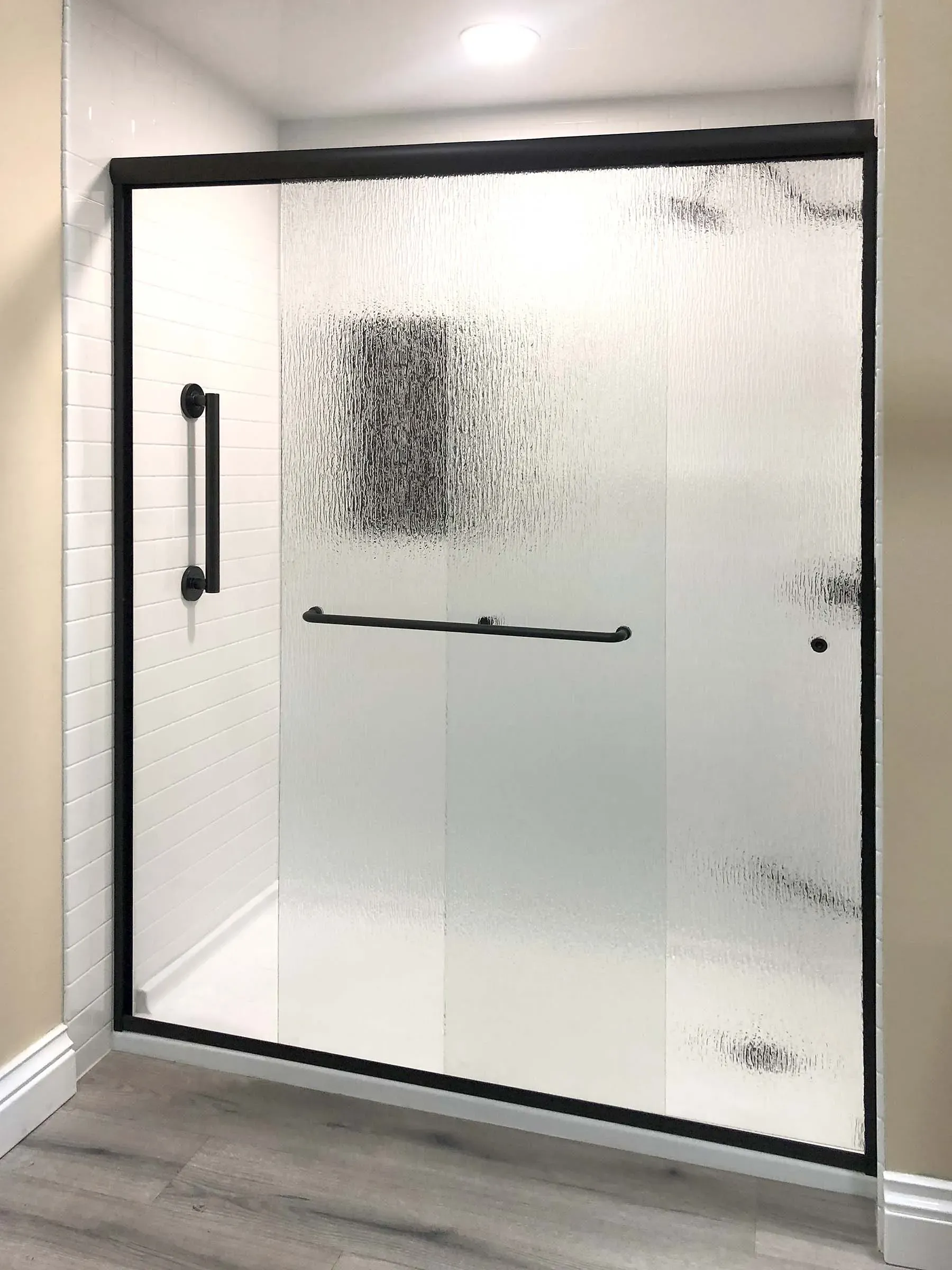A beige bathroom with a walk-in shower with privacy sliding glass doors and black fixtures.