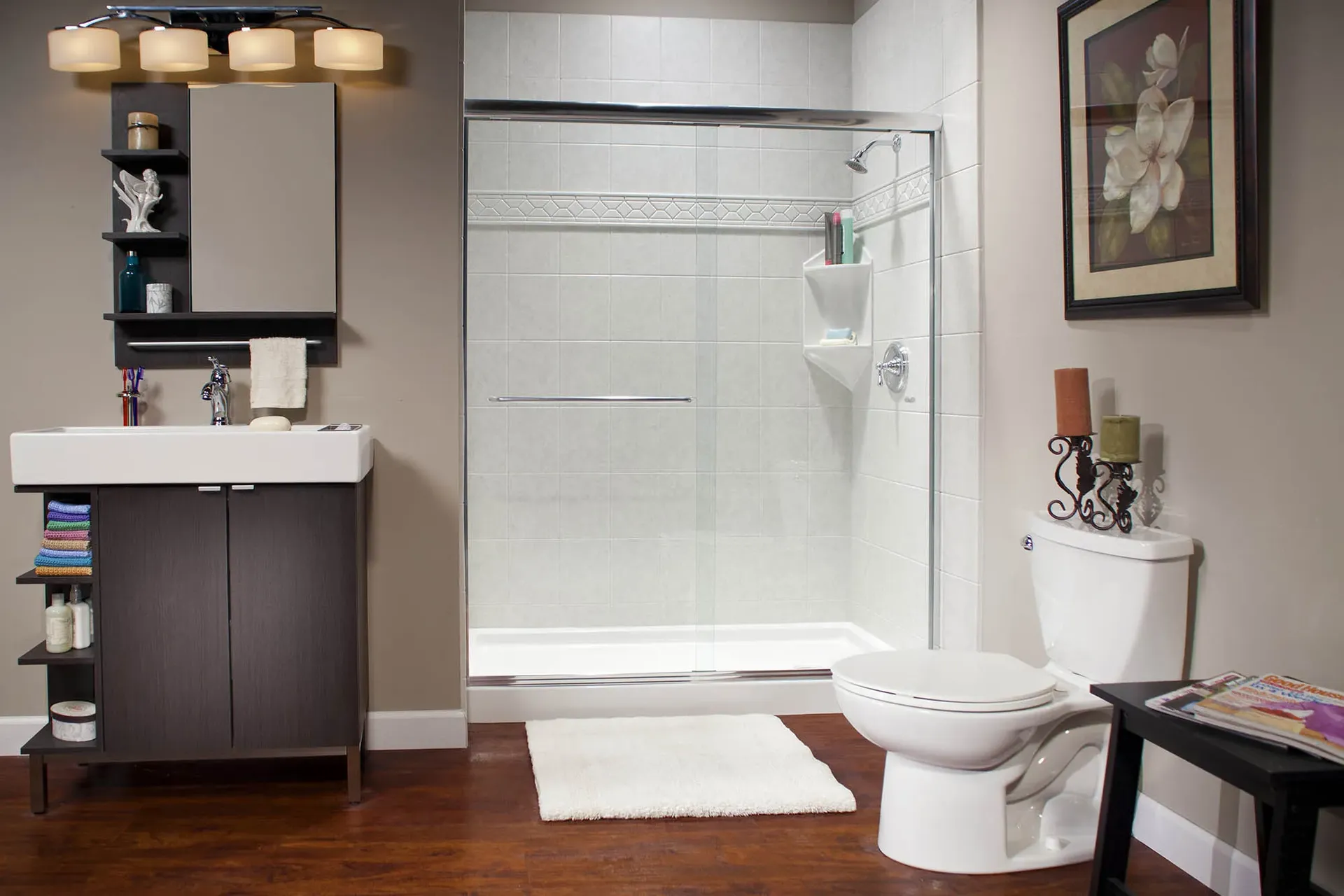A gray bathroom with dark wood floors, walk-in shower with sliding glass doors, and white tile walls.