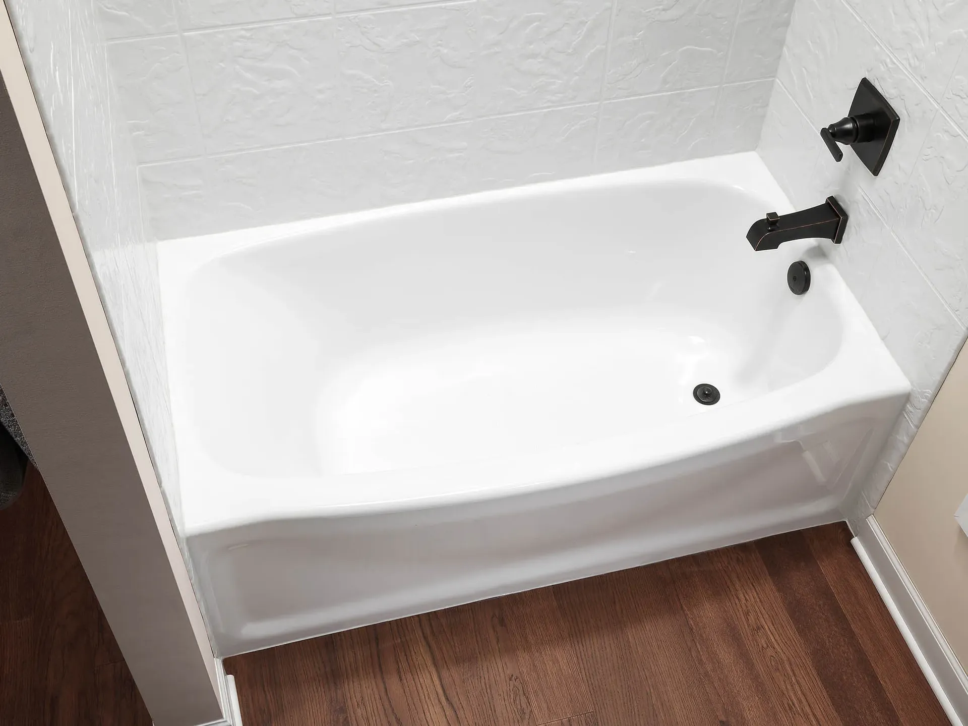 An overhead view of a white converted bathtub with black fixtures and white textured walls.