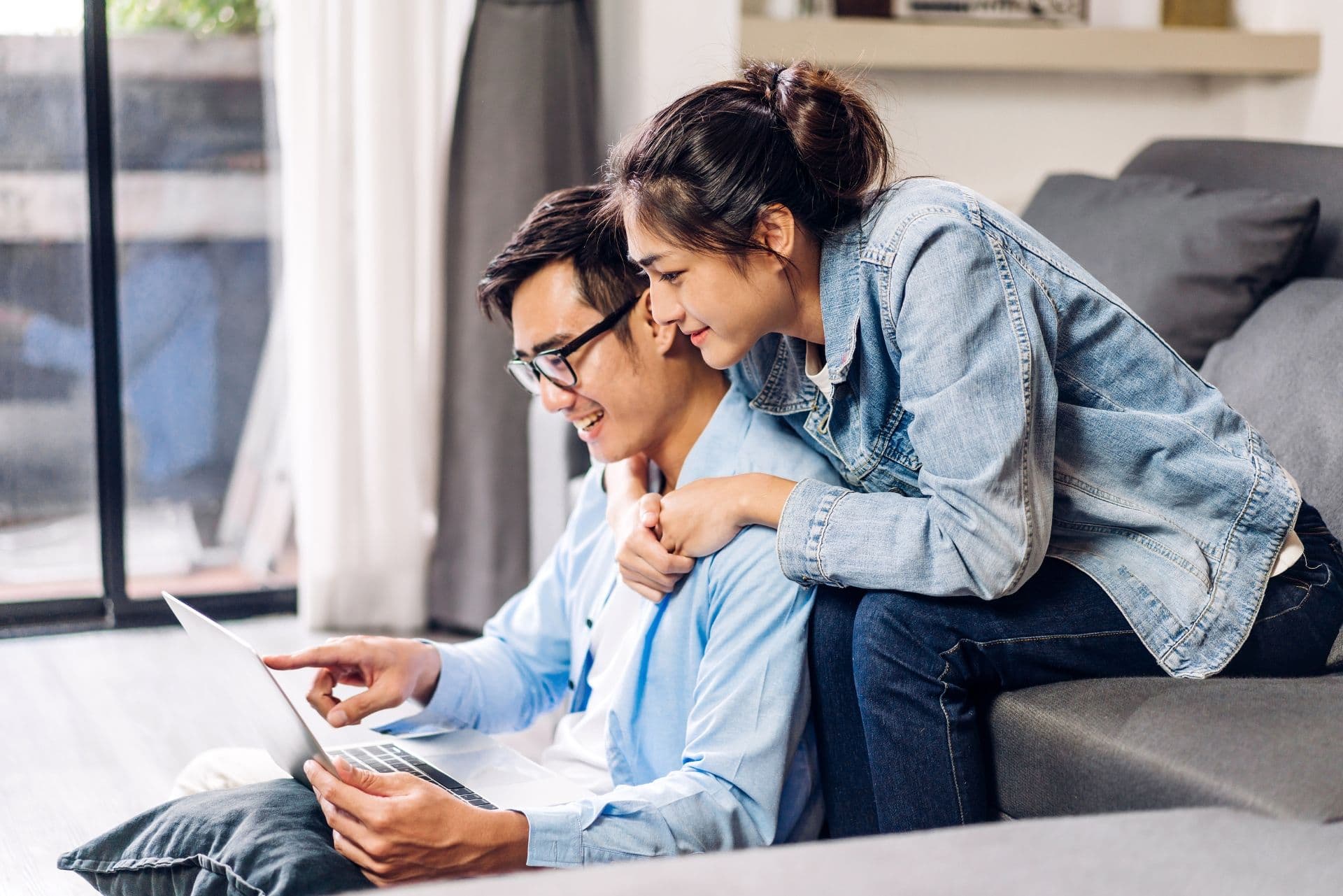 A couple sit on a couch and look at a laptop.
