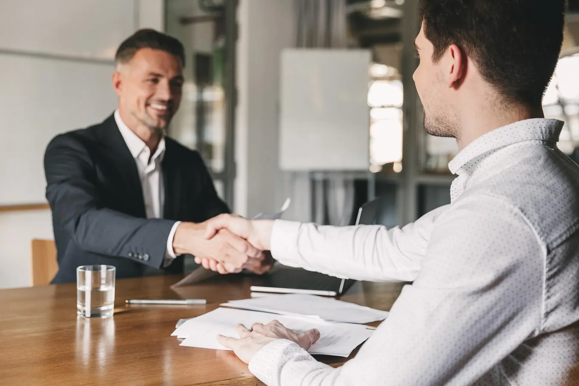Two professionals shake hands across a desk.