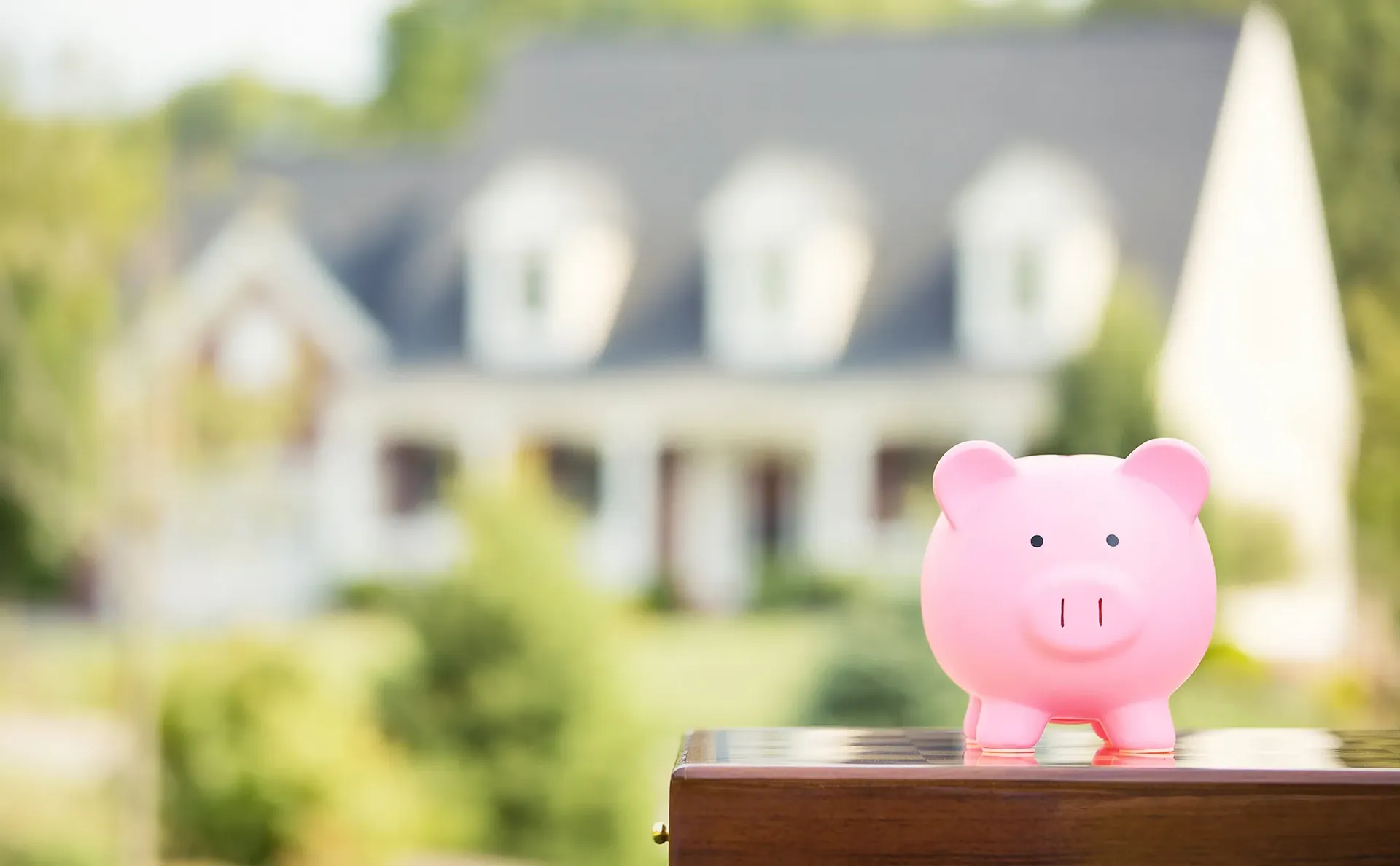 A piggy bank sits on a post in the foreground; a house is visible in the background.