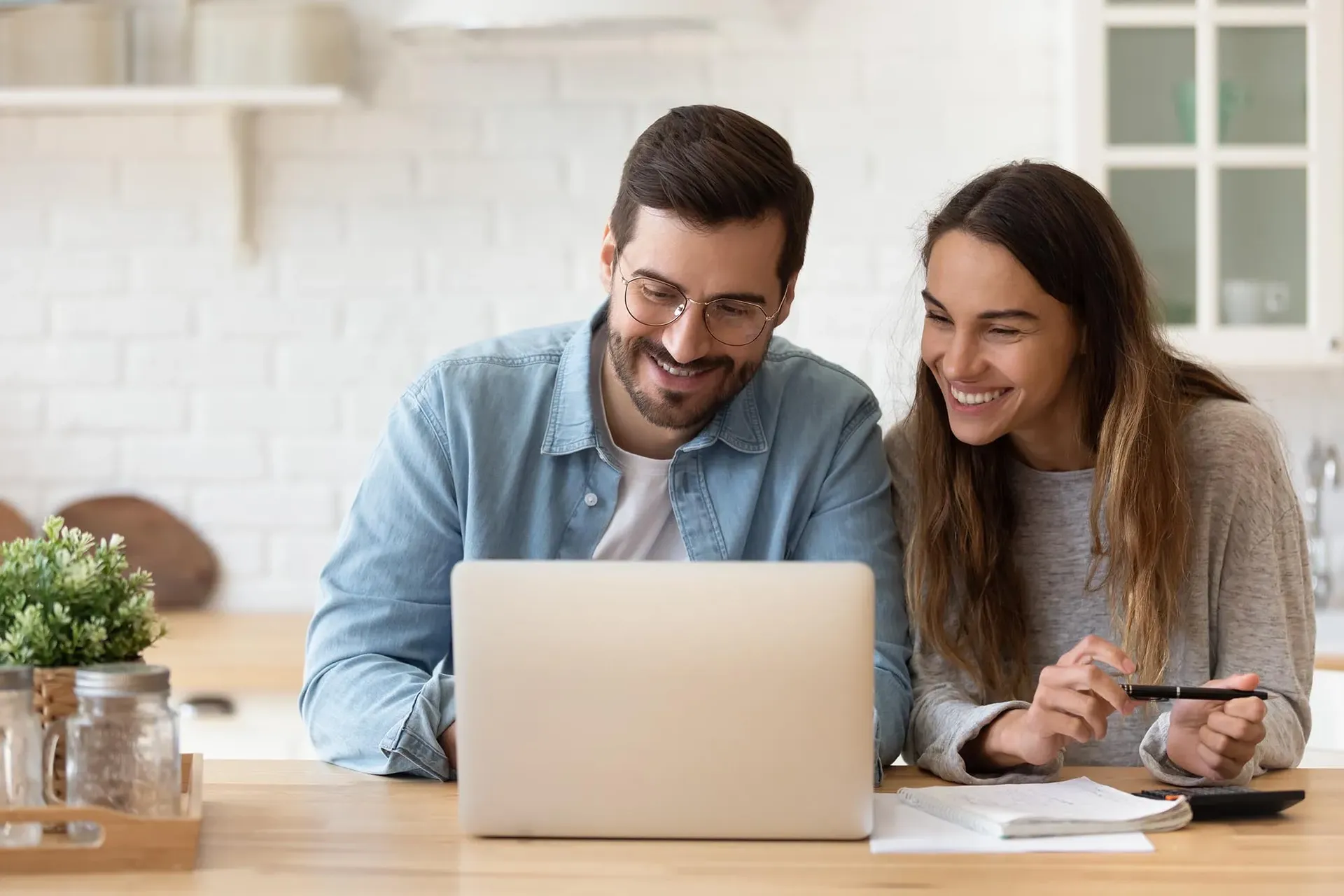A couple smiles sitting in front of a laptop.
