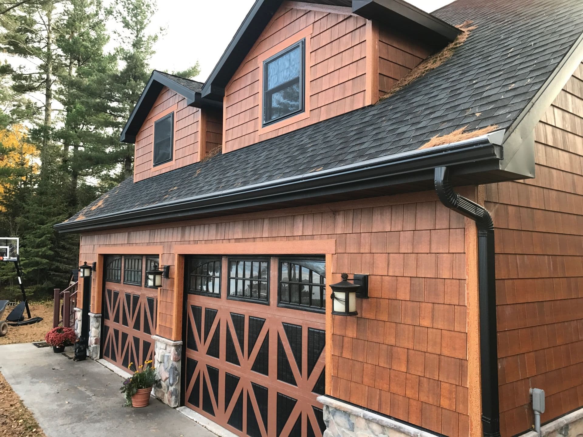 A rich brown shingled house with black roof and new black gutters and downspout.