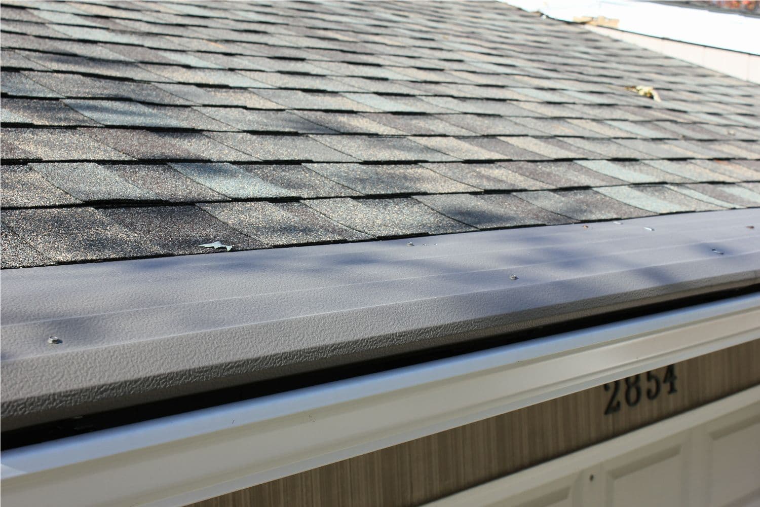A close-up of new, bronze-colored Gutter Helmet gutter covers on a house with a gray roof.