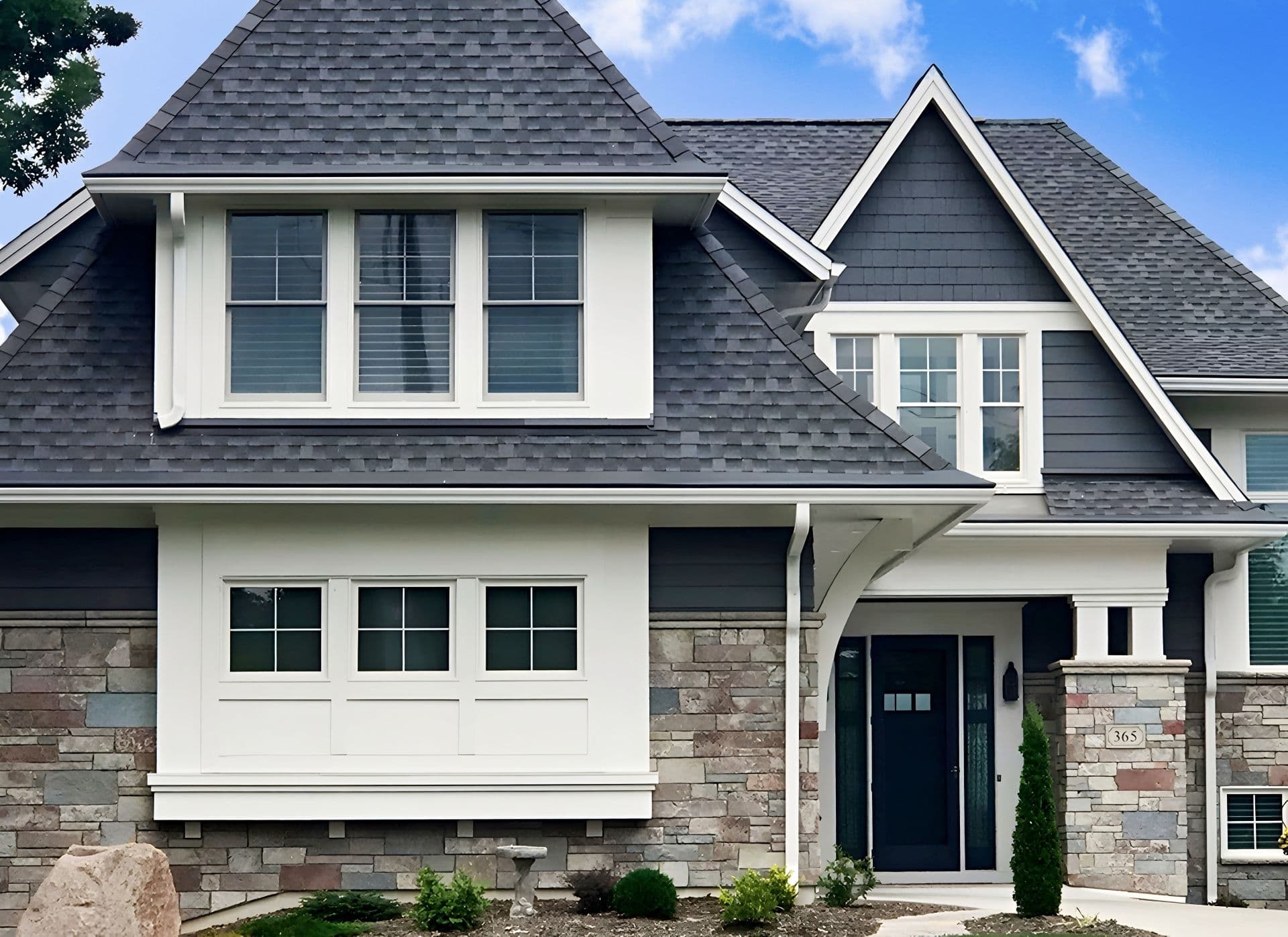 The front of a stone house with new black Gutter Helmet gutter covers and white gutters and downspout.