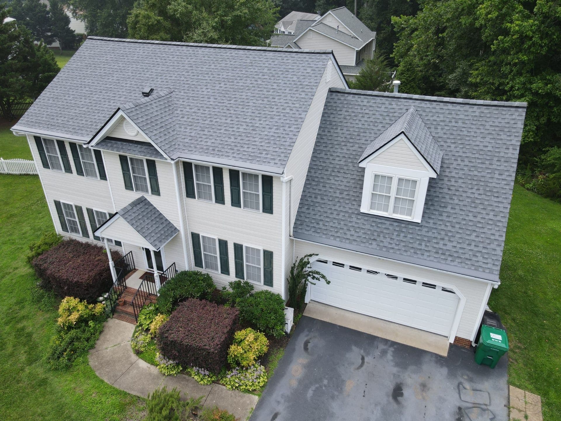 An aerial view of a white house with dark green shutters, light gray roof, and new gutters with gutter covers.