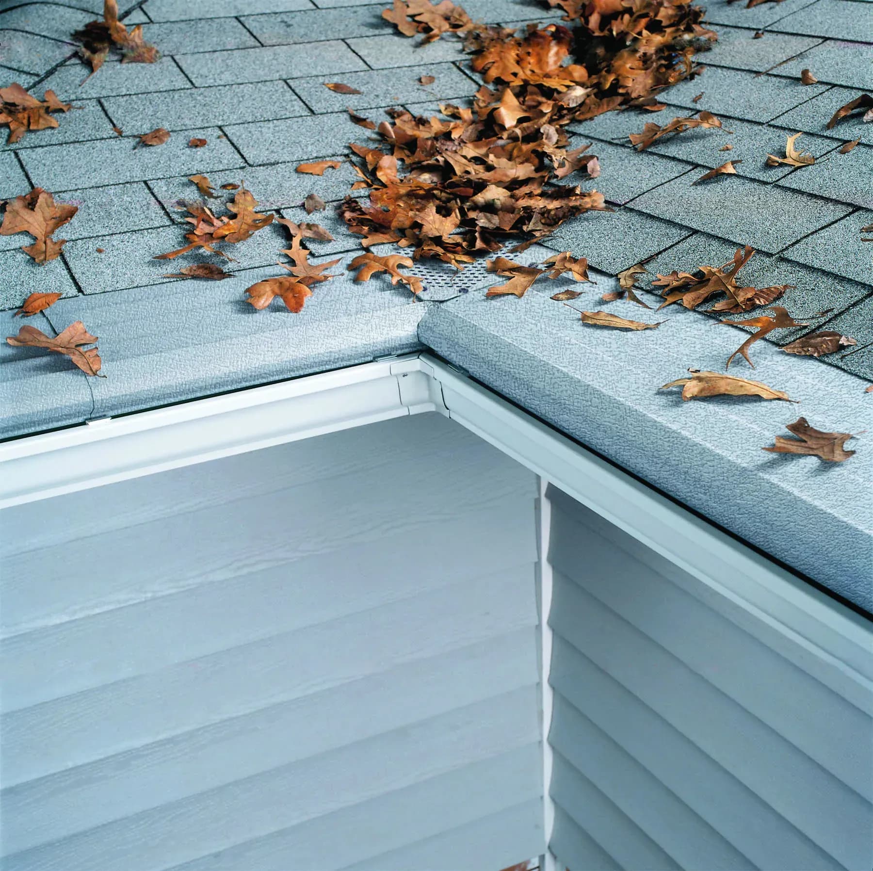 A close-up of a corner of a house with white gutters and light gray gutter covers.