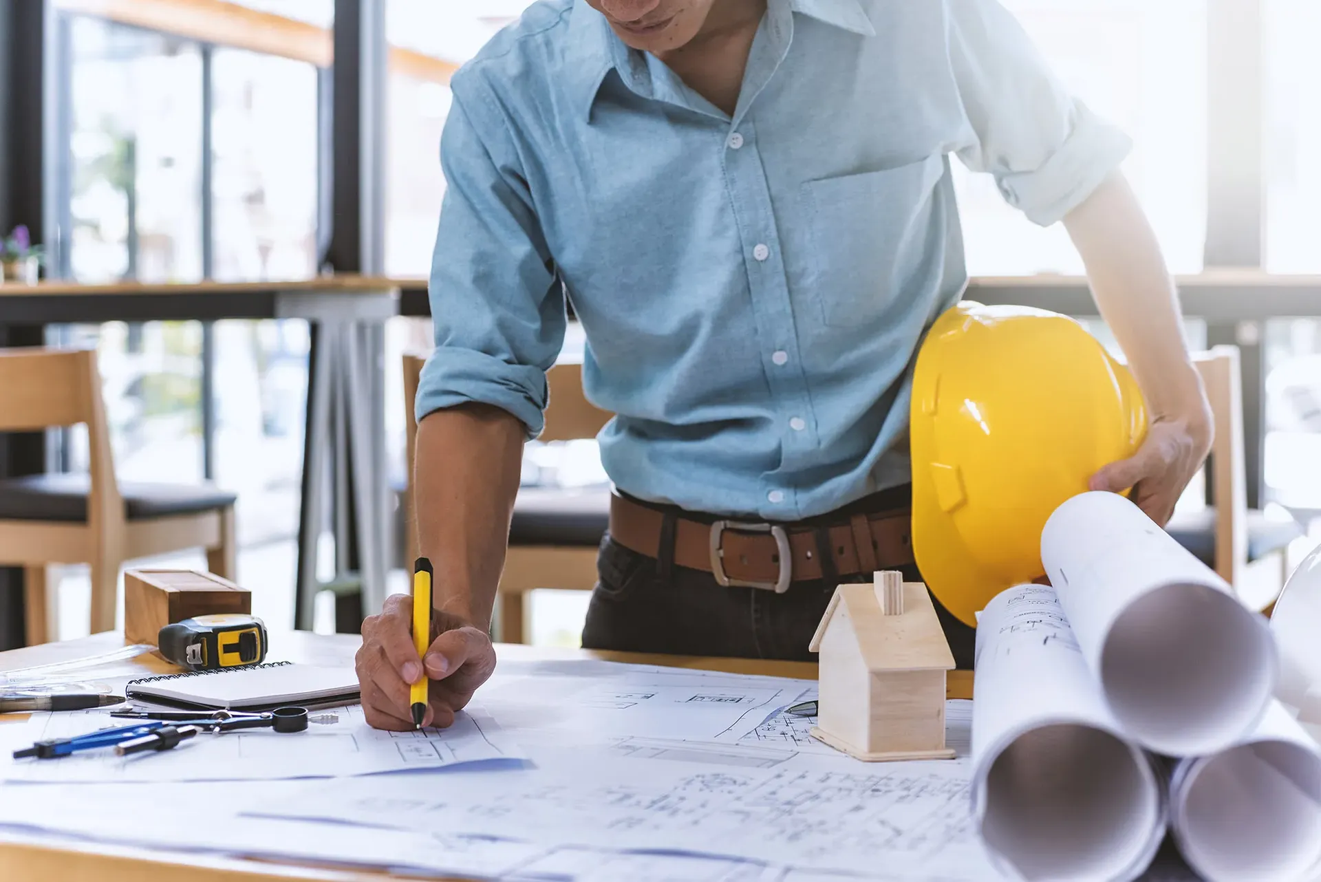 A worker holding a yellow hard hat marks up a blueprint.