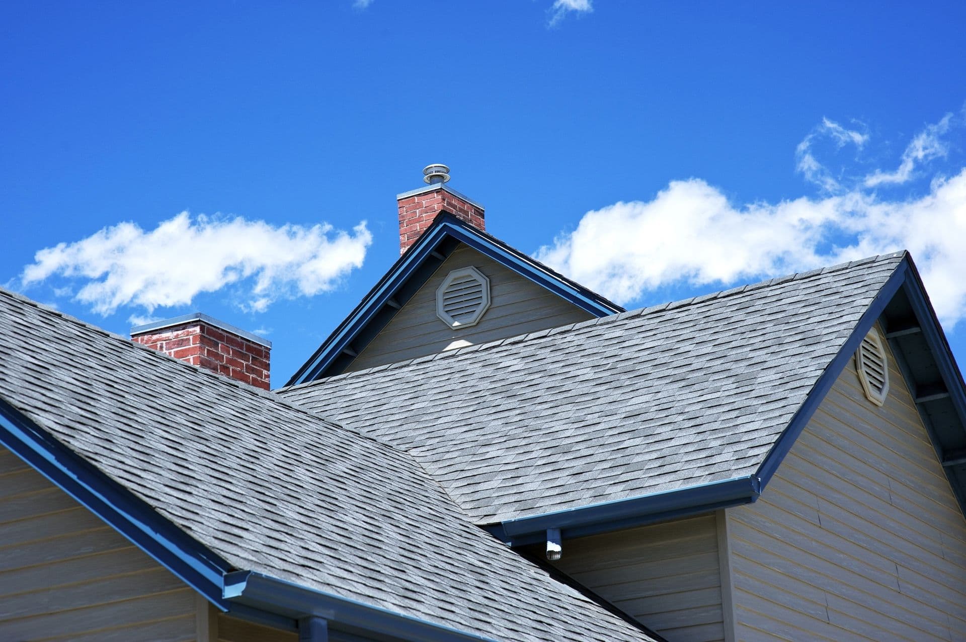 A gray house with new gray roof and blue gutters.