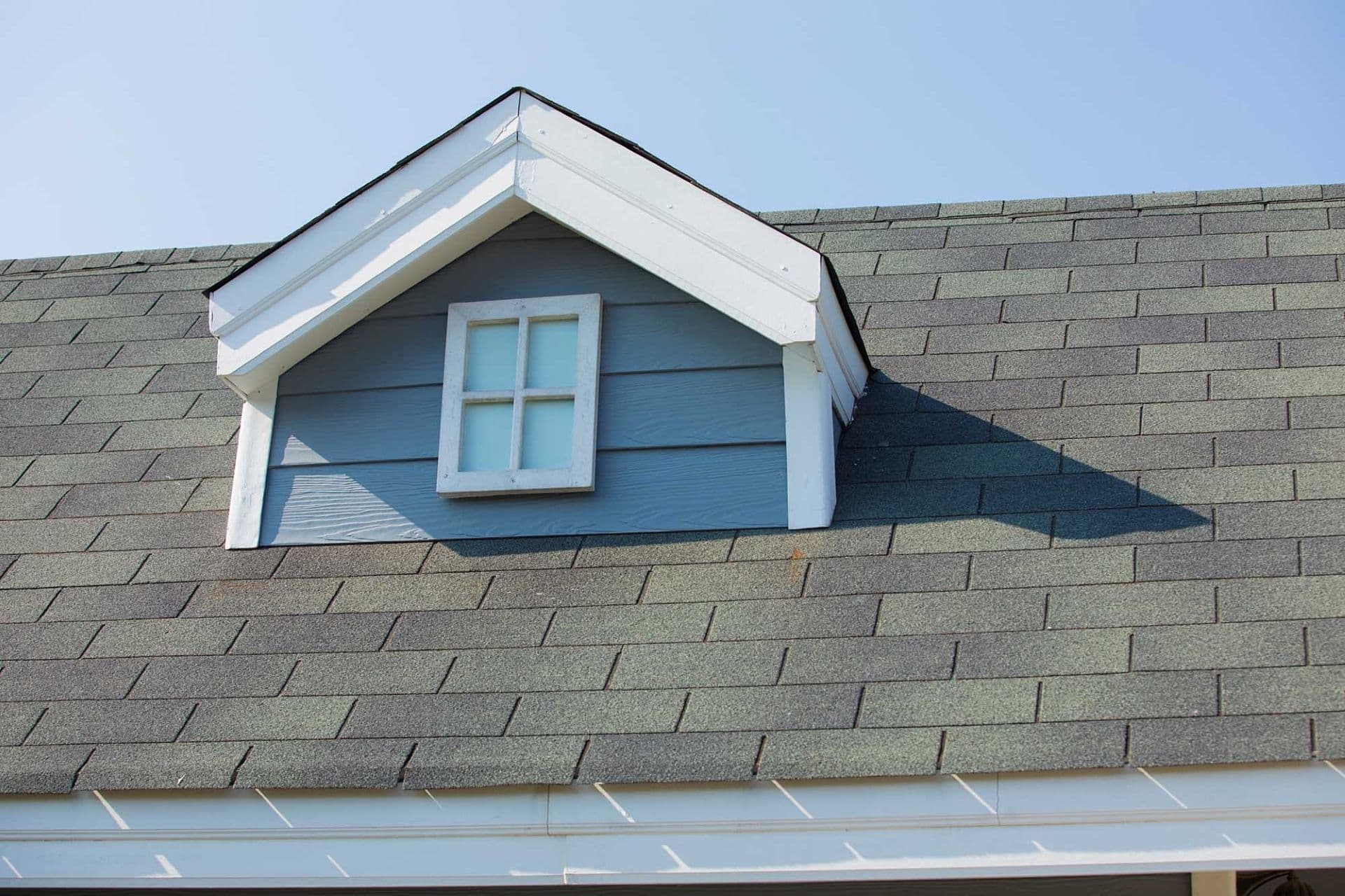 A blue house with a small eave and black shingle roofing.